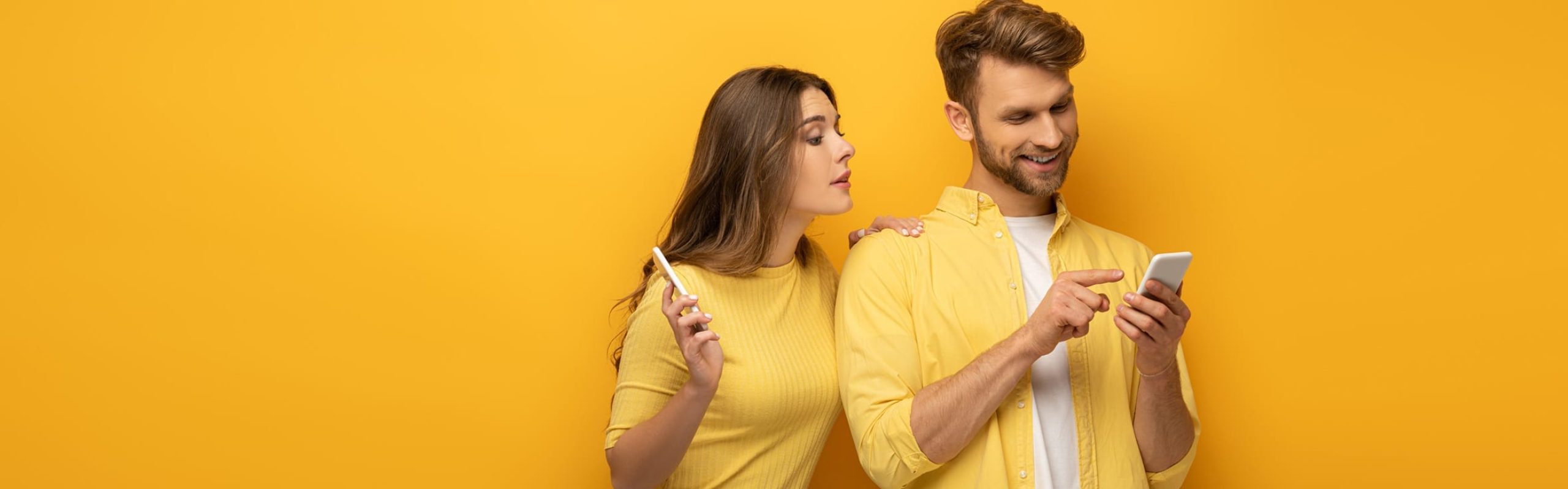 une femme et un homme tiennent leurs téléphones à la main. L'homme pointe son doigt vers son propre téléphone et les deux portent leur attention sur l'écran.